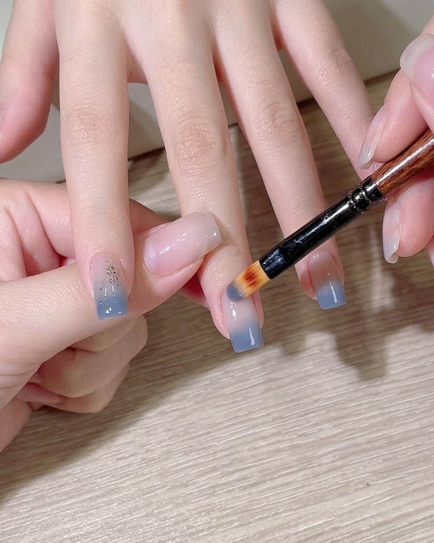 Una spugnetta per il trucco che tampona smalto azzurro su ununghia.