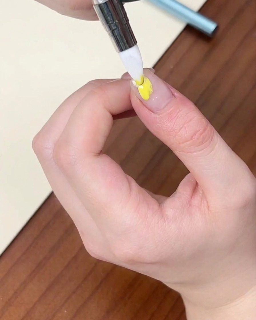 Un pennellino di precisione applica una goccia di smalto gel giallo su ununghia naturale.