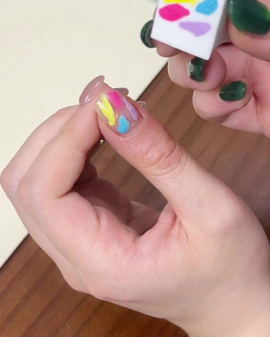 Unimmagine ravvicinata che mostra il lato di una spugnetta usata per sfumare gocce di gel multicolore sullunghia.
