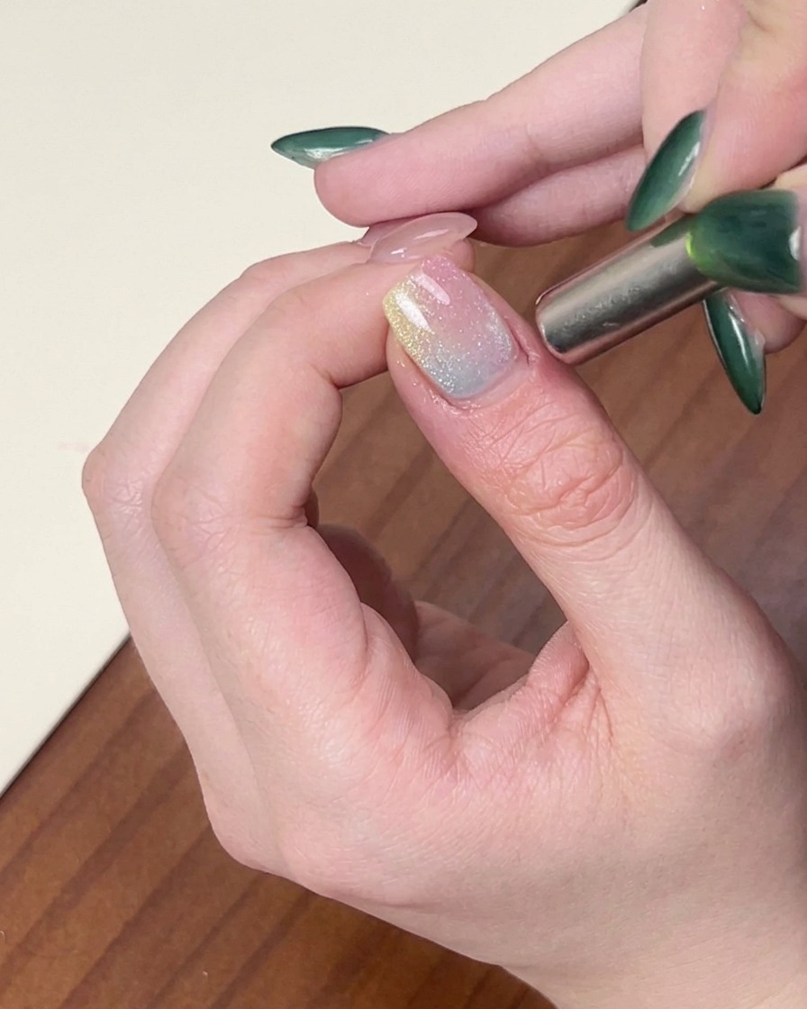 Un magnete cilindrico tenuto vicino al lato di ununghia per modellare lo scintillante smalto gel cat-eye.