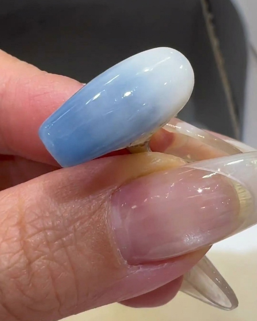 Un pennello applica un sottile strato di smalto gel bianco latte su una tip trasparente.
