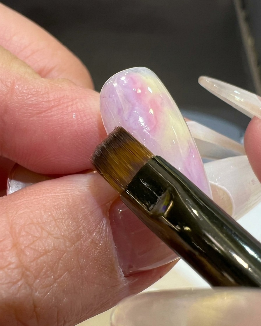 Un pennello piatto applica un colore gel rosa-viola semitrasparente nellangolo di una tip con base bianca.