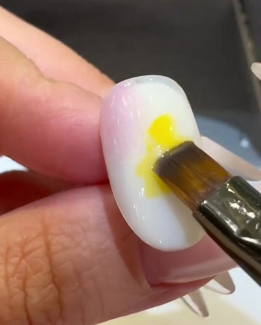 Un pennello piatto posiziona una goccia di smalto gel giallo brillante al centro dellunghia.
