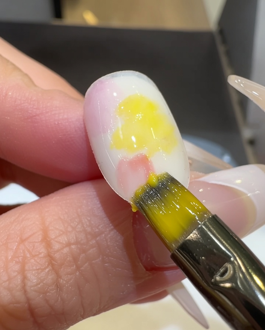 Un pennello piatto sfuma lo smalto gel rosa e giallo sulla superficie dellunghia.