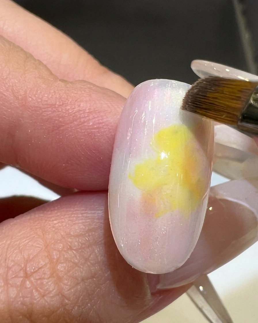 Un pennello piatto uniforma la sfumatura tra lo smalto gel rosa e giallo su una tip.