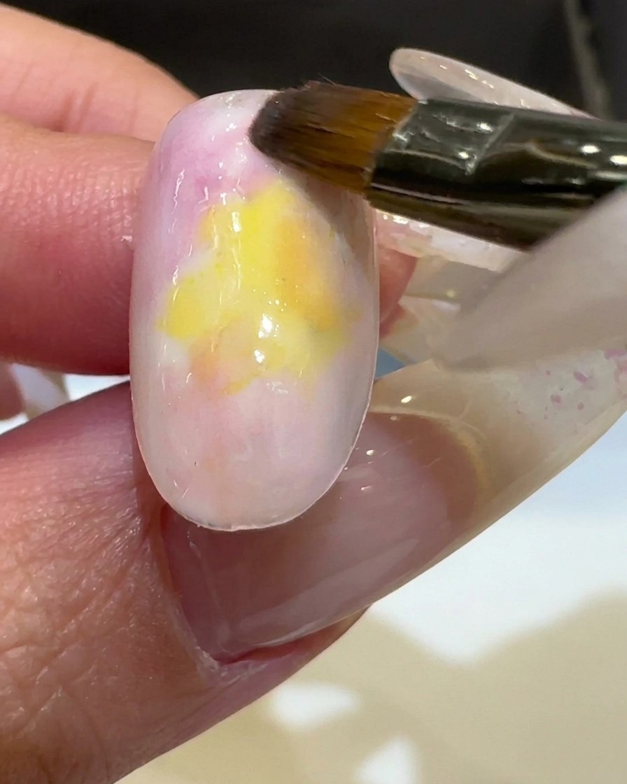 Un pennello applica uno smalto gel giallo vibrante al centro dellunghia, sfumandolo nei colori esistenti.