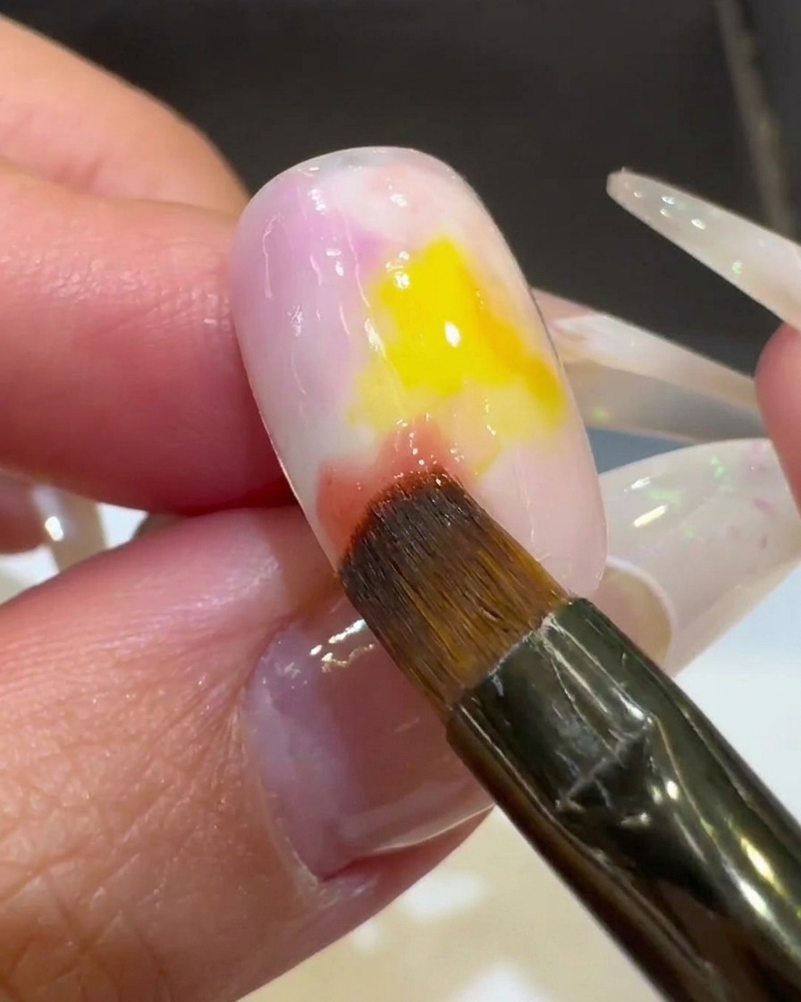 Primo piano di un pennello che sfuma lo smalto gel rosa nel centro giallo, creando un effetto gradiente.