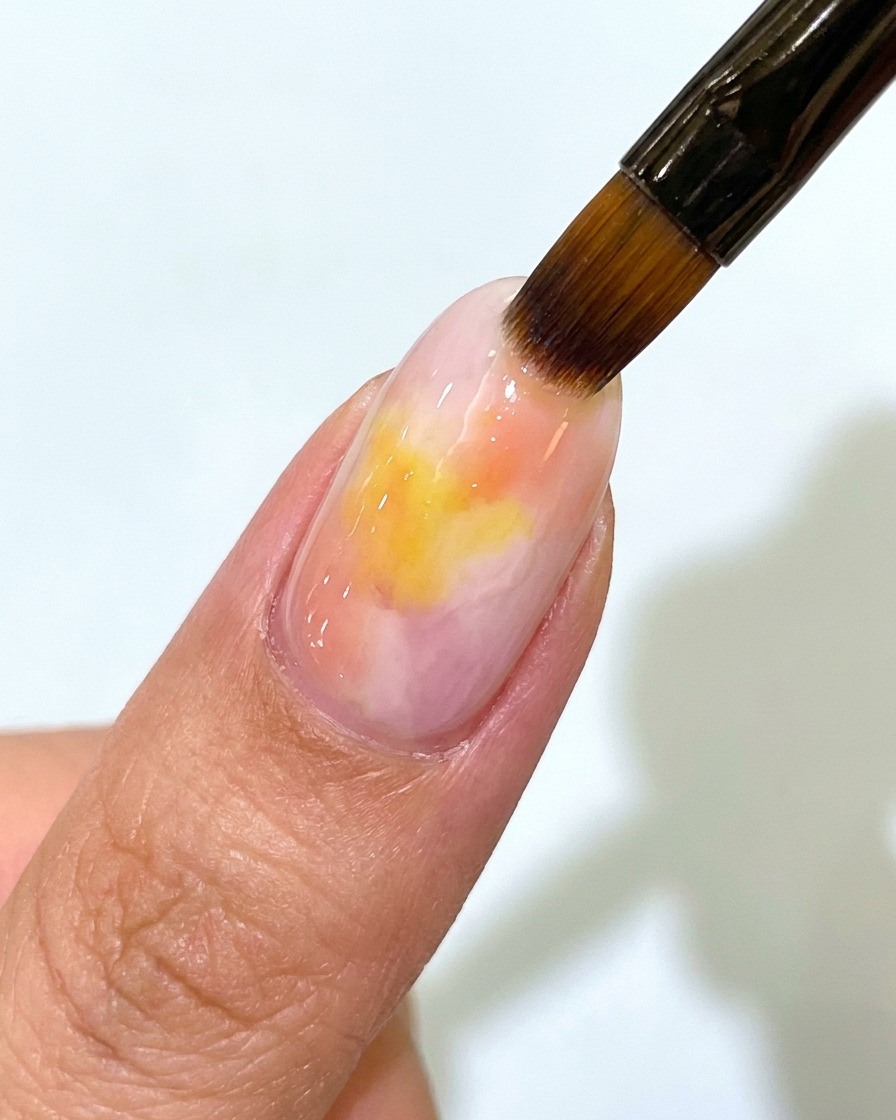 Un pennello per unghie applica un top coat opaco trasparente sopra ununghia in gel con sfumatura rosa e gialla.