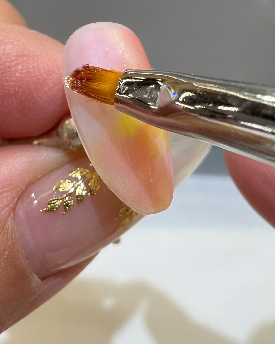 Un pennello liner sottile applica una linea spessa di gel trasparente 3D su ununghia opaca color tramonto.