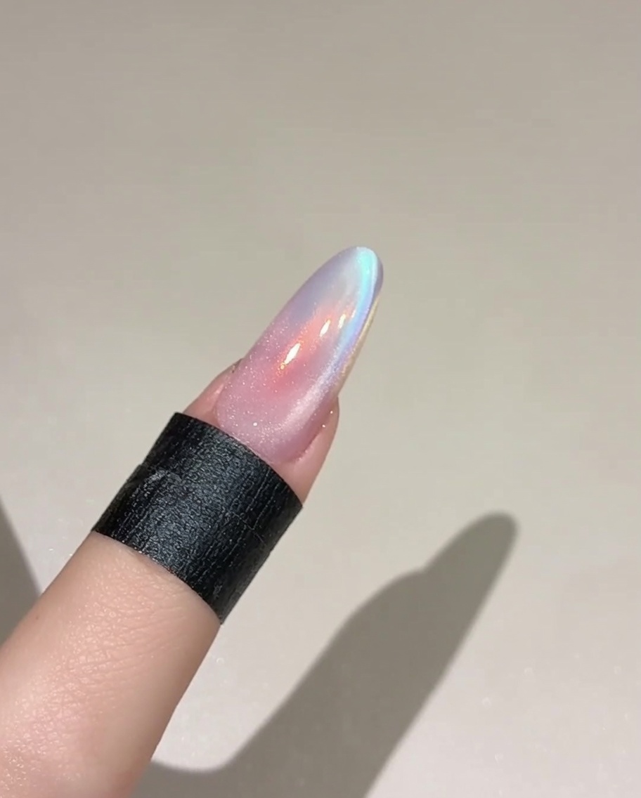 Un pennello che applica uno strato di gel cat eye traslucido e scintillante su ununghia dipinta con un colore di base.