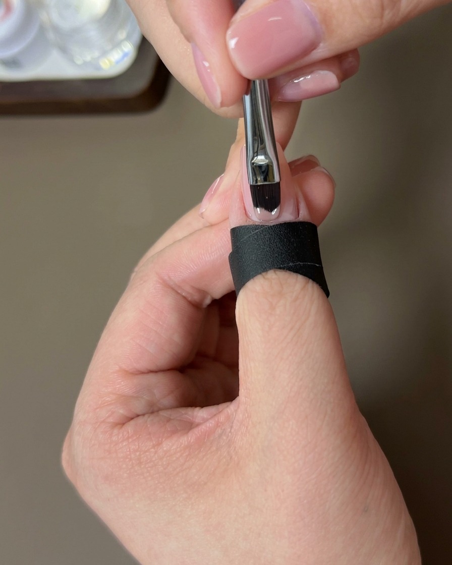 Un pennello applica uno strato di smalto gel nude sullunghia naturale.
