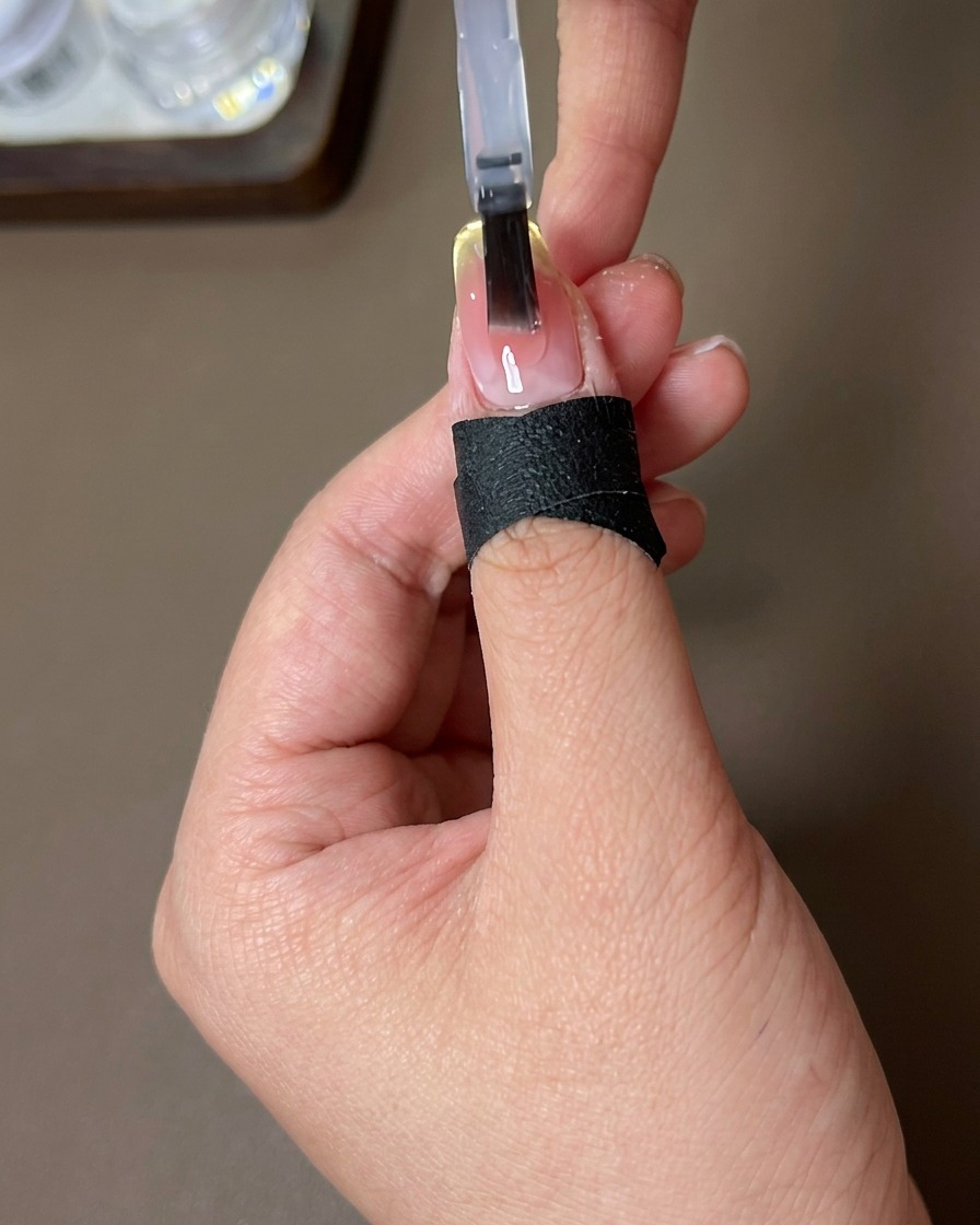 Un pennello applica un top coat lucido e trasparente su ununghia con gradiente blush ed effetto magnetico.