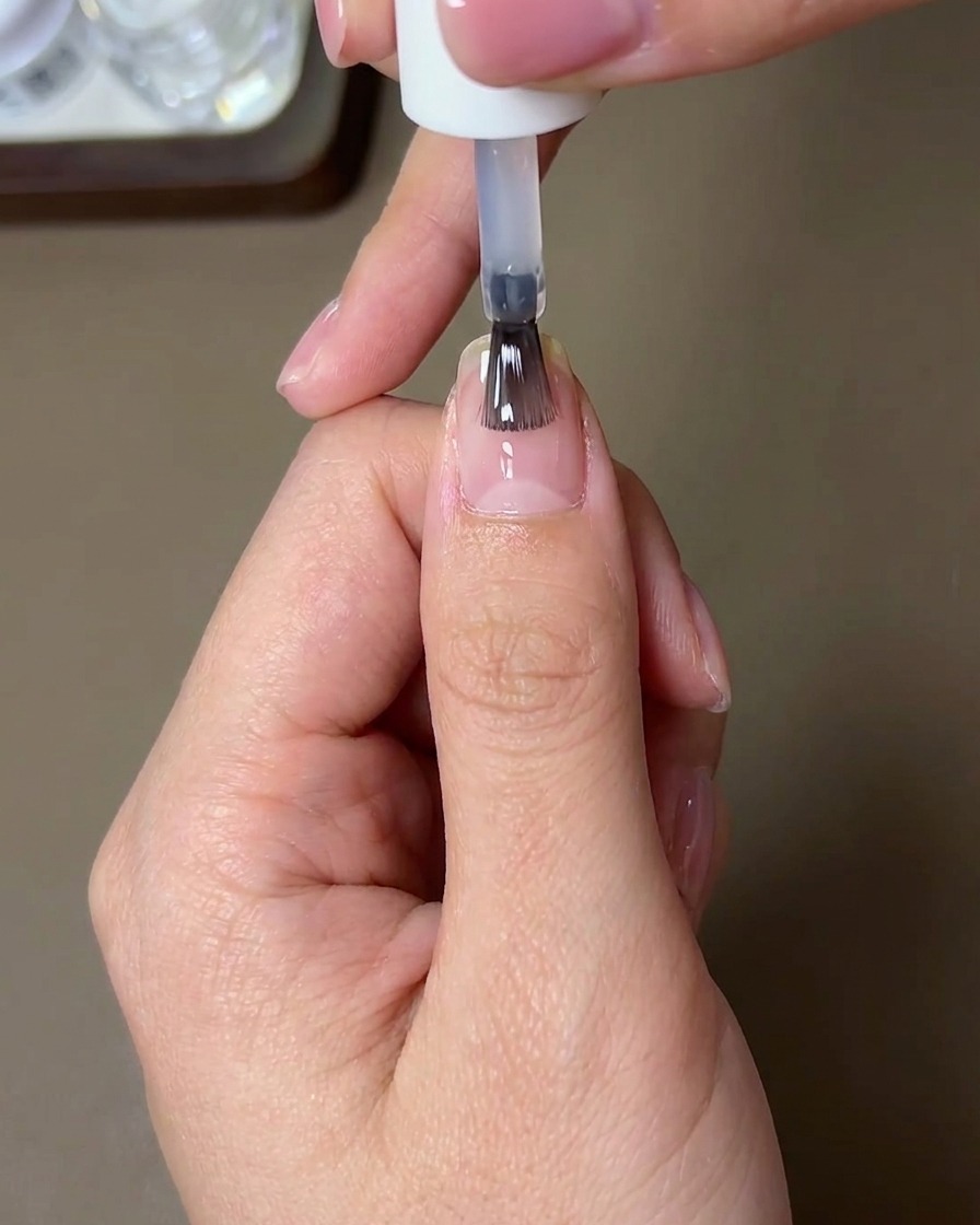 Un pennello applica un top coat rinforzante lucido su ununghia rifinita con polvere aurora.