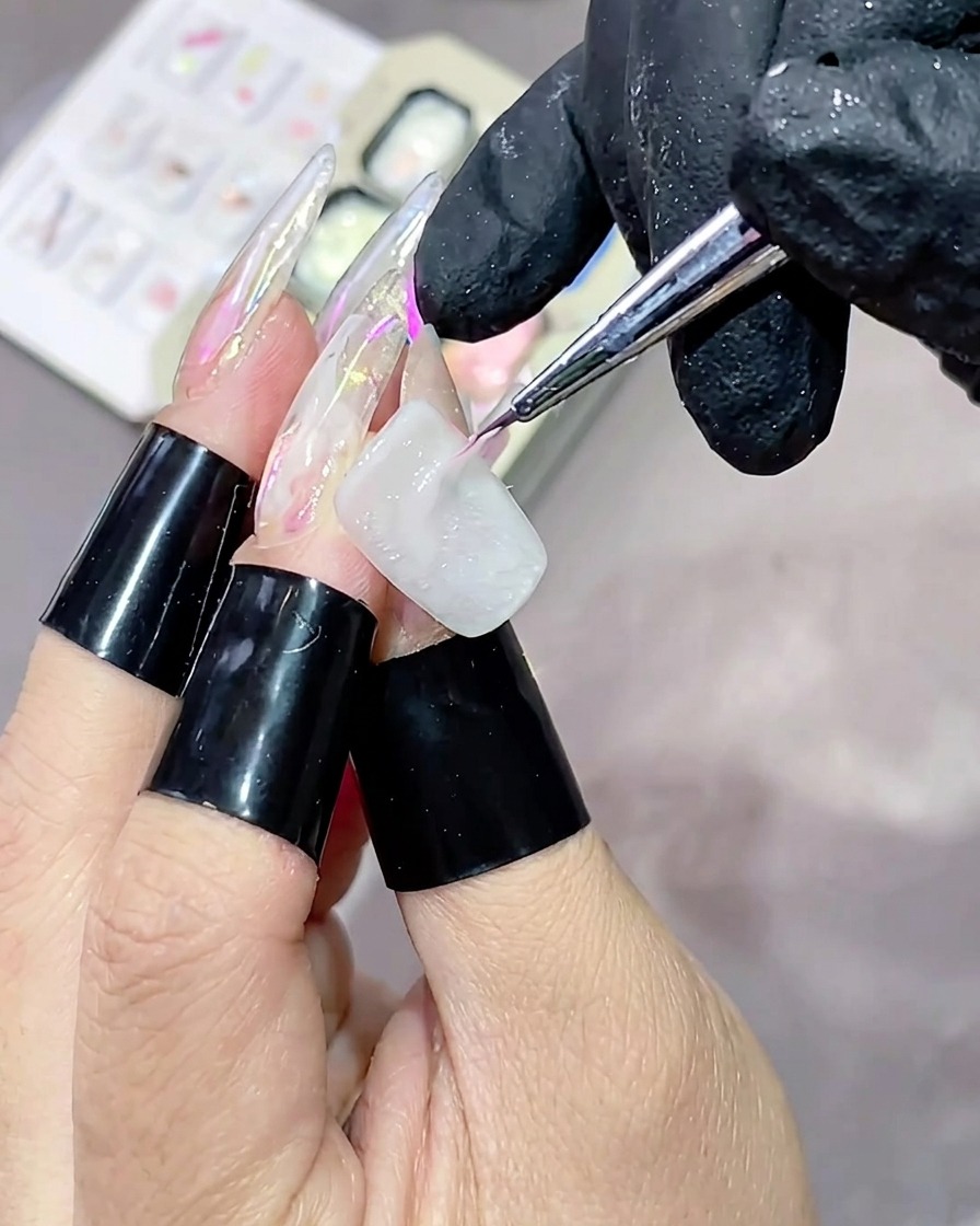 Un pennello liner sottile che applica una striscia orizzontale di gel testurizzato rosa lucido su ununghia laccata di bianco.