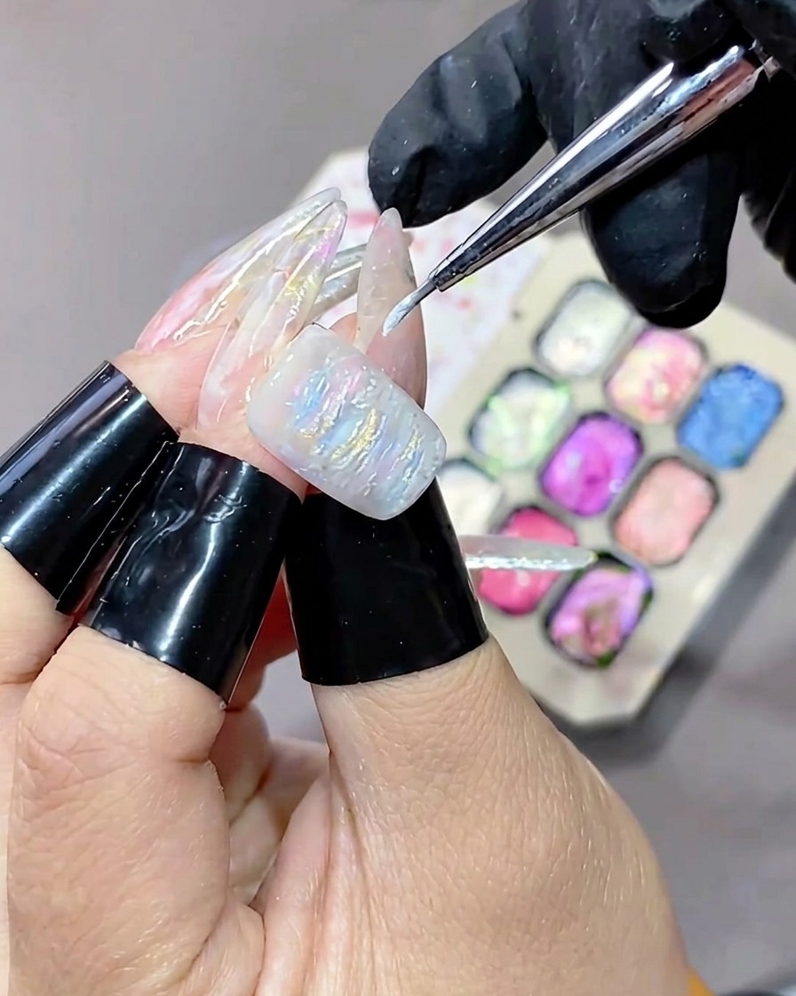 Un pennello a punta fine che applica gel bianco illuminante sulla superficie testurizzata di una manicure in gel.