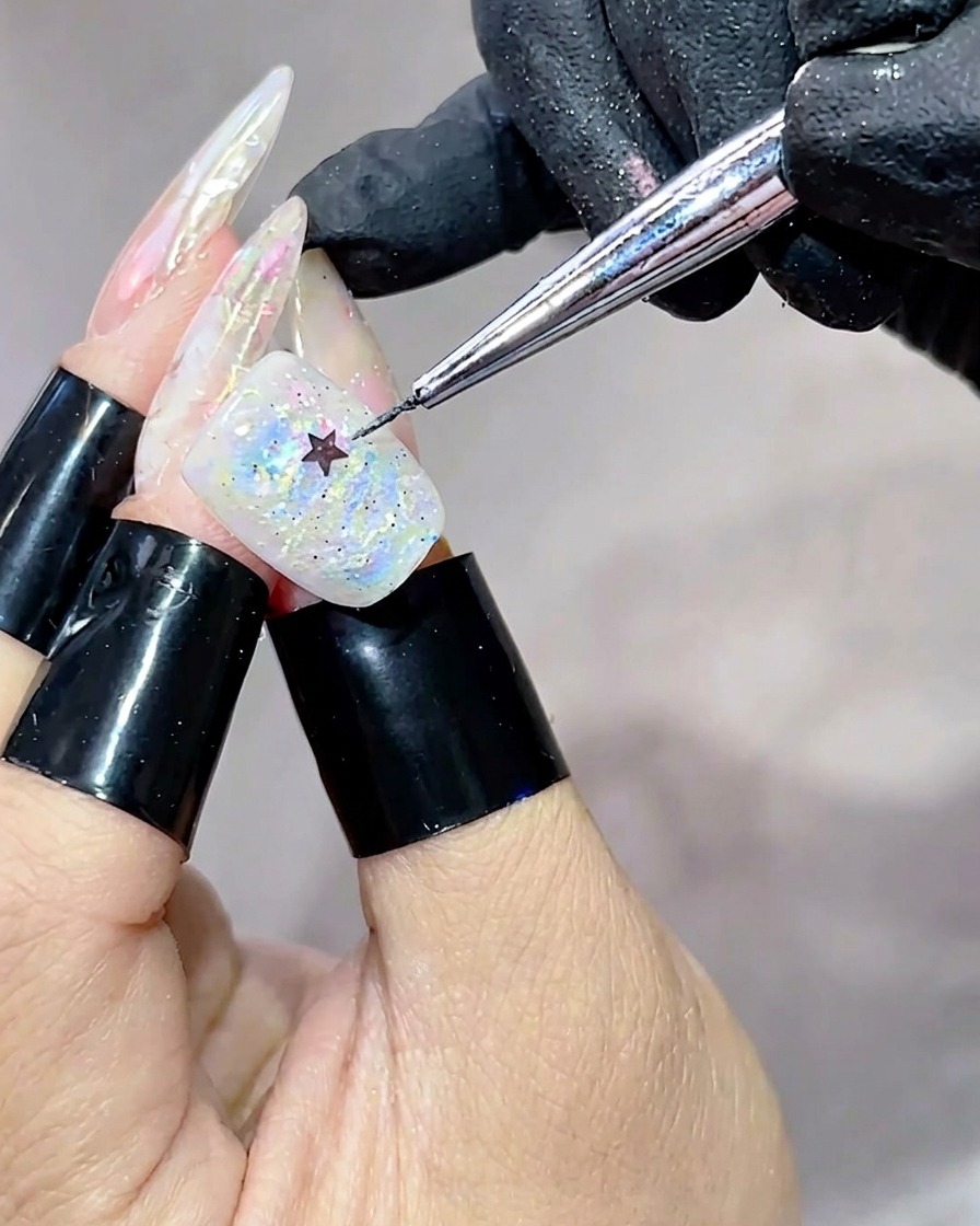 Uno strumento di metallo che posiziona una piccola paillette a forma di stella nera al centro di ununghia coperta di gel iridescente e multicolore.
