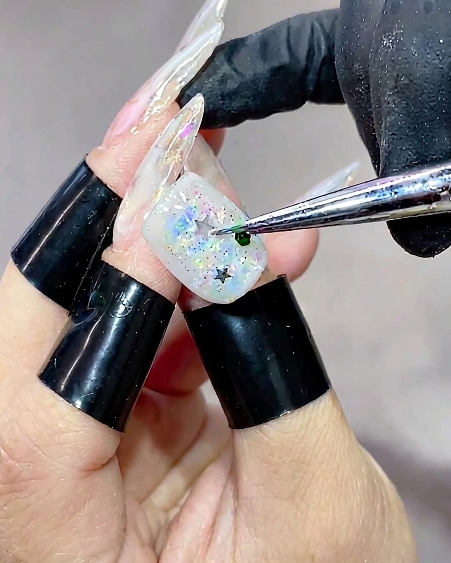 Primo piano di uno strumento che posiziona una piccola paillette esagonale verde sulla superficie dellunghia già decorata con glitter a stella.