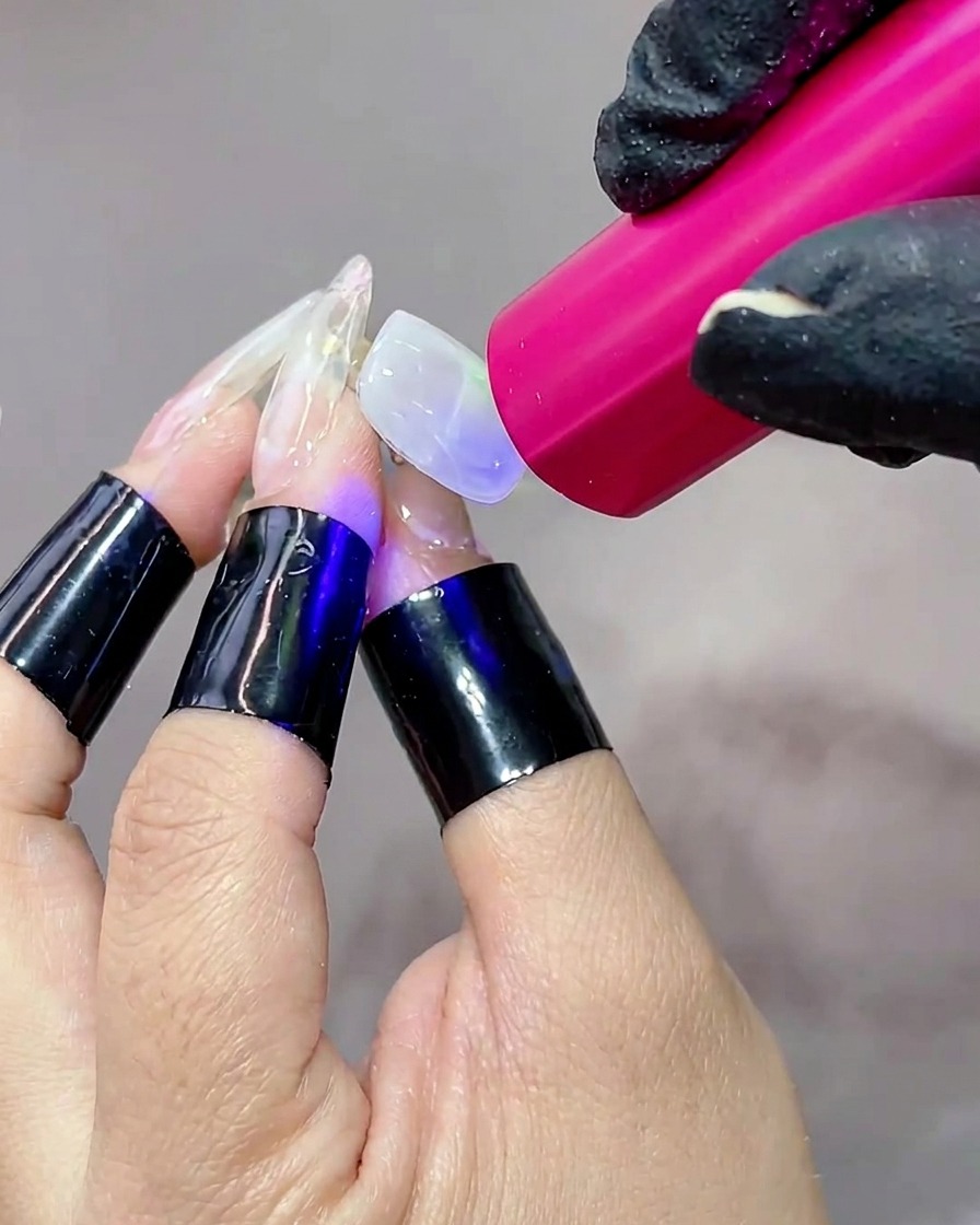 Una mano posizionata sotto una lampada UV portatile, con la superficie dellunghia illuminata durante la polimerizzazione del gel.