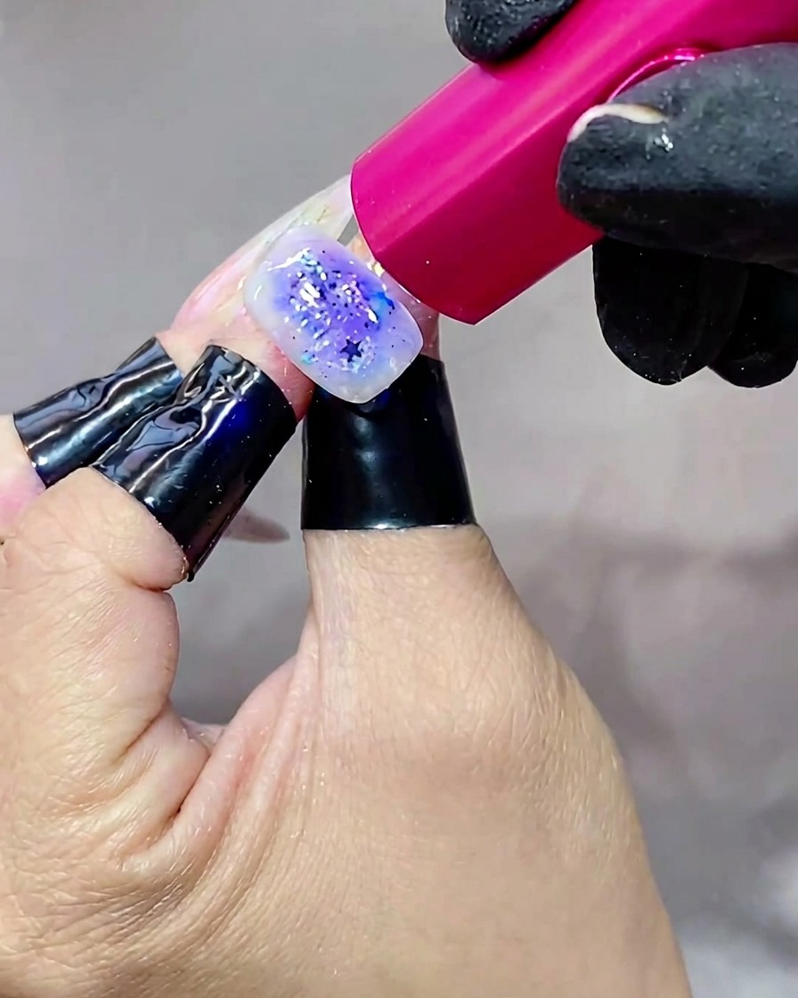 Una mano che tiene ununghia sotto una brillante lampada UV, polimerizzando lo strato finale di top coat.