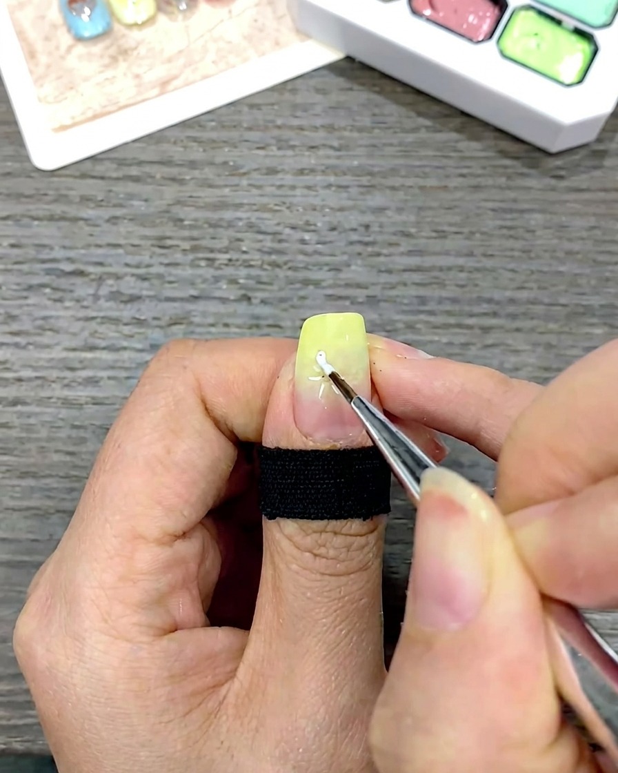 Un pennello liner fine che disegna i petali di una margherita bianca tirando il gel verso il centro dellunghia.