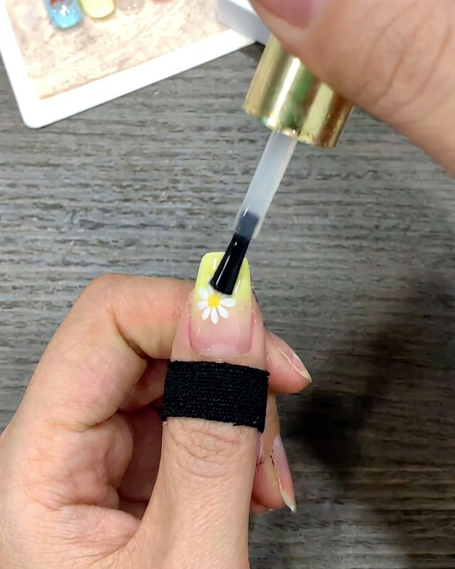Scatto ravvicinato di un pennello per unghie che leviga uno strato di top coat lucido sullintera superficie dellunghia.