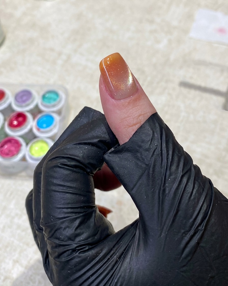 Una mano con guanto nero usa pinzette per tenere un piccolo applicatore a spugna, picchiettando delicatamente gel arancione sulla punta dellunghia.