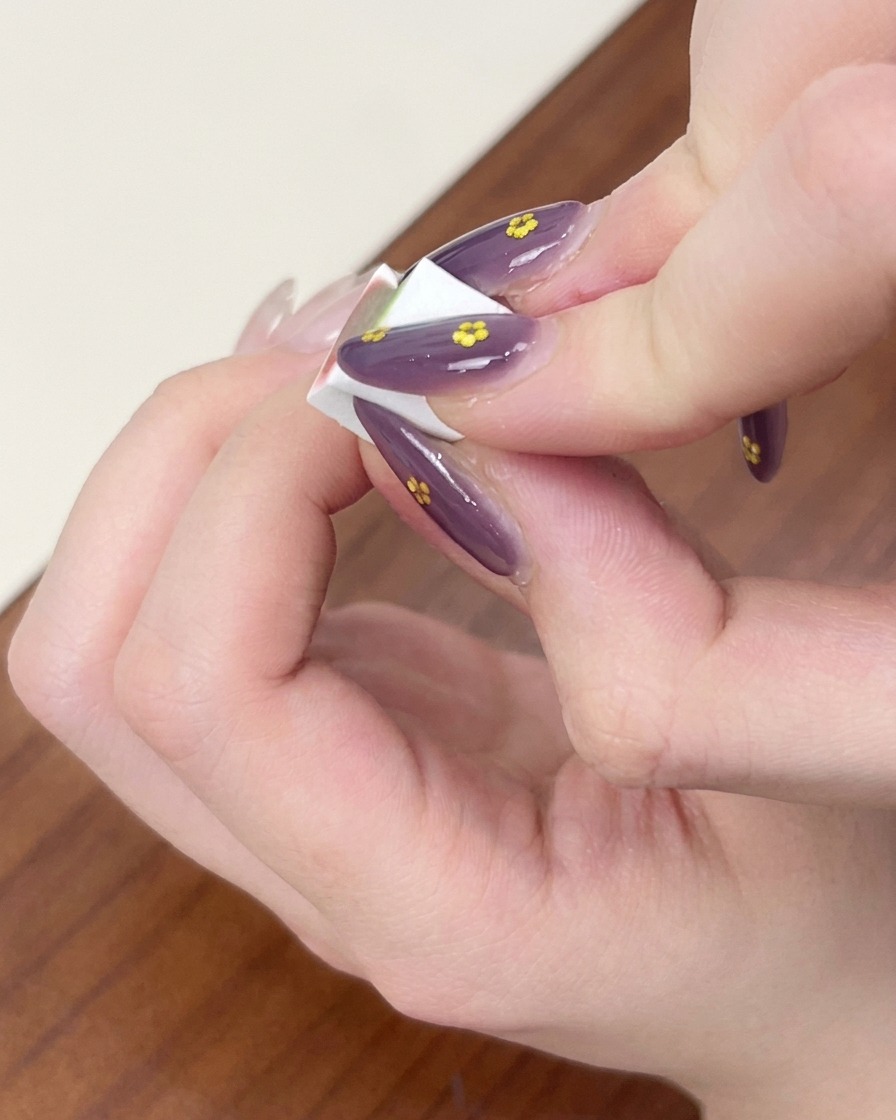Dita che tengono una piccola spugnetta da trucco bianca, picchiettando e sfumando lo smalto gel azzurro per un effetto ombré su ununghia.
