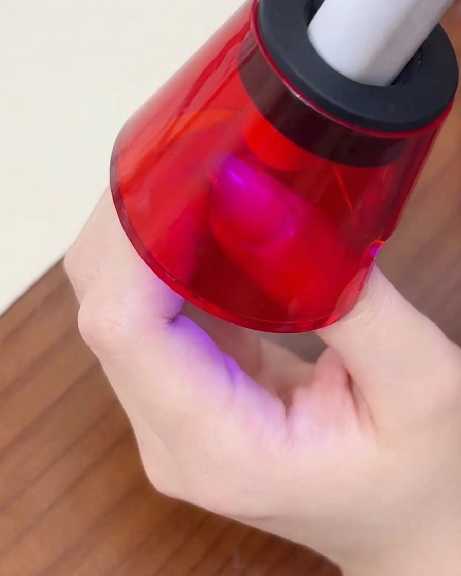 Un dito posto sotto una mini lampada UV portatile rossa per polimerizzare lo smalto gel.