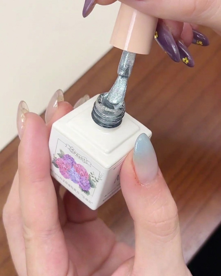 Un pennello per smalto gel applica uno strato di gel cat-eye argentato brillante su ununghia con sfumatura azzurra.