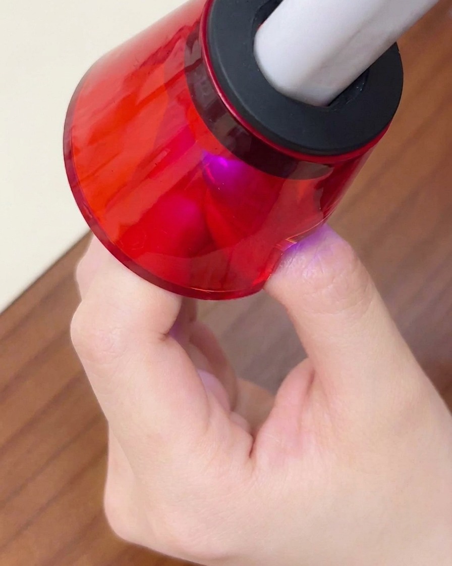 Primo piano di un dito posto sotto una mini lampada UV/LED rossa portatile per la polimerizzazione finale.