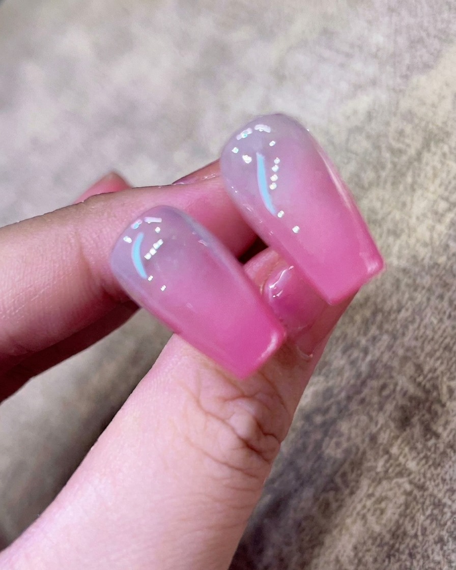 Primo piano dellapplicazione di un base coat trasparente con un pennellino su ununghia naturale pulita.
