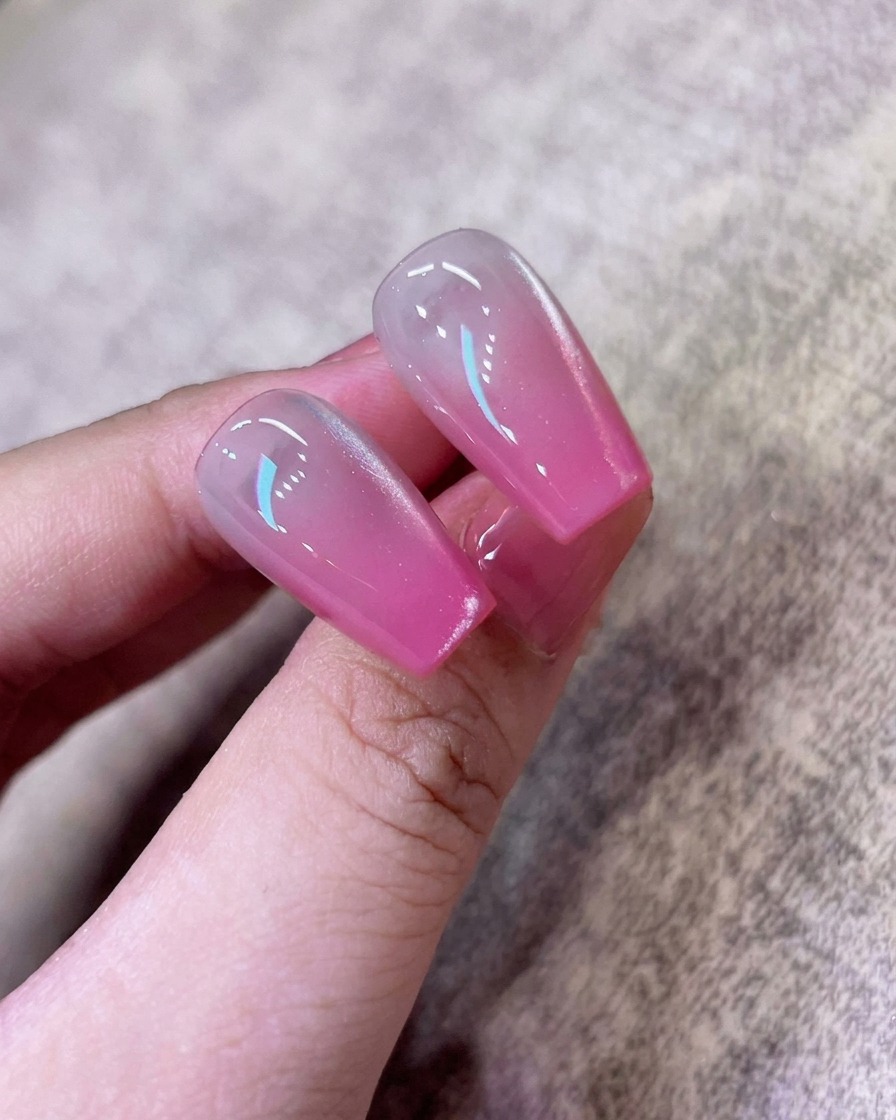 Un pennello applica uno strato di smalto gel cat-eye bianco perlato sopra lunghia con ombrè rosa.