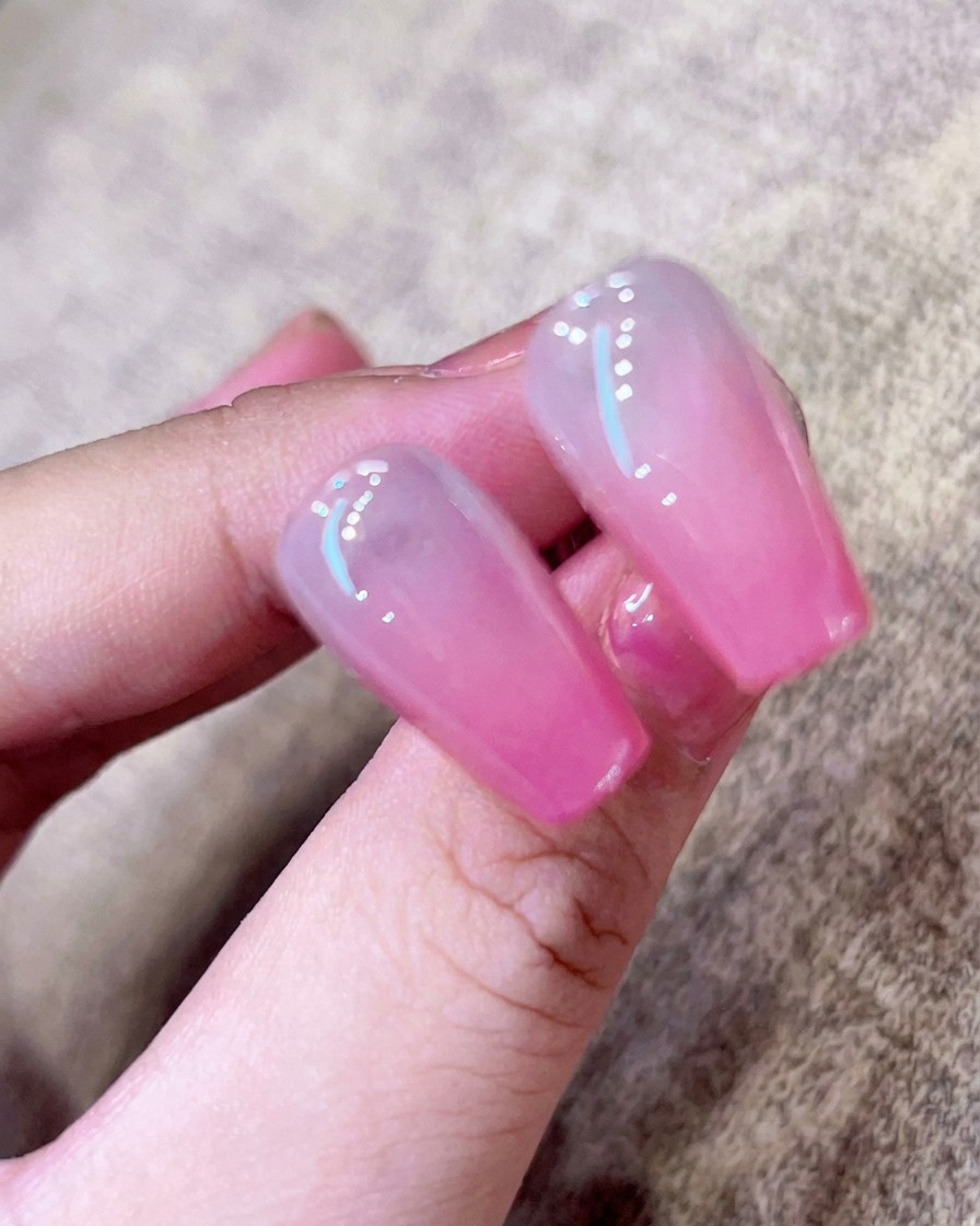 Primo piano di un pennello che applica un top coat trasparente e lucido su ununghia ombrè rosa.