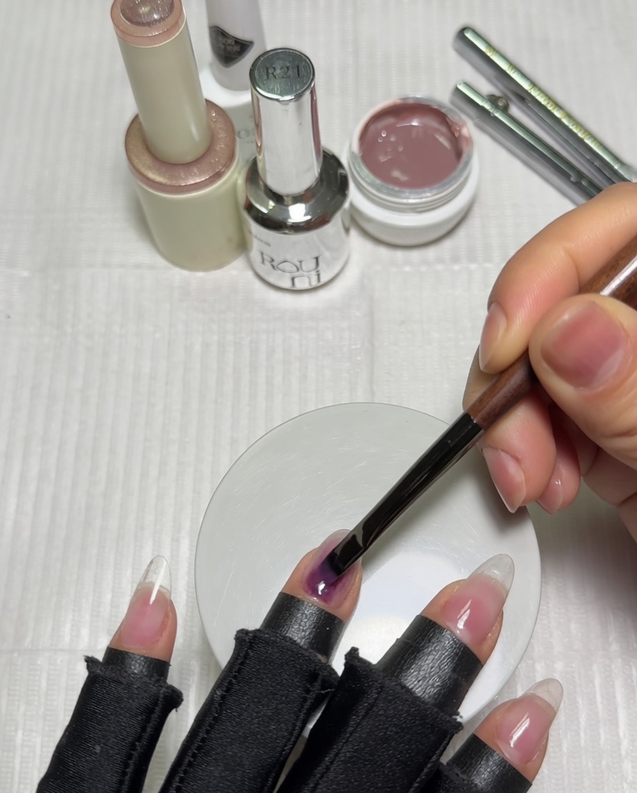 Una mano posizionata allinterno di una lampada UV viola con base gel color nude sulle unghie.