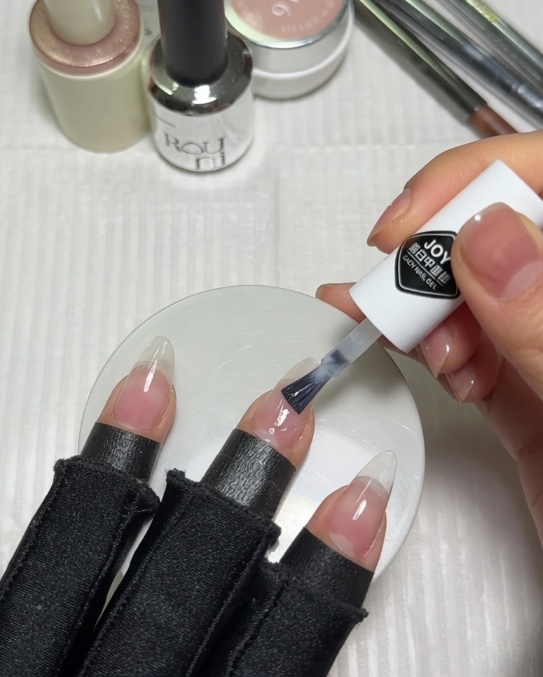 Applicazione di smalto gel bianco latte sulla metà superiore di ununghia nude rosata preparata.