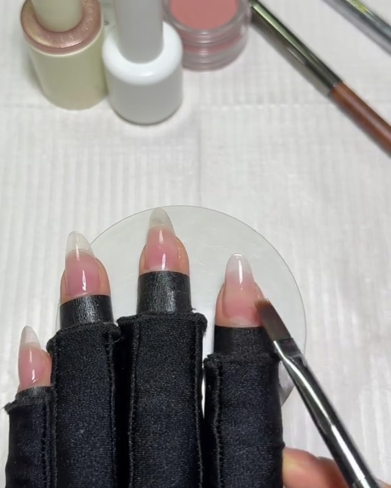 Un pennello piatto per sfumature scorre orizzontalmente sullunghia per miscelare il bordo del gel bianco latte nella base nude.