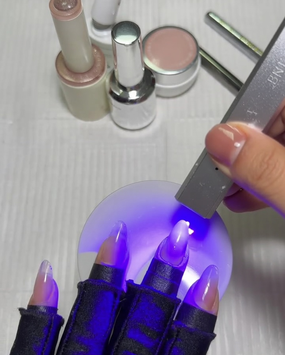 Una mano con manicure sfumata posta allinterno di una lampada UV/LED, polimerizzando sotto luce viola.