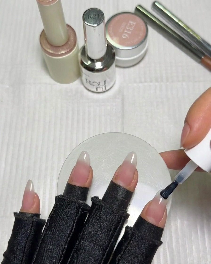 Un pennello applica una piccola quantità di smalto gel bianco latte sulla punta di ununghia.