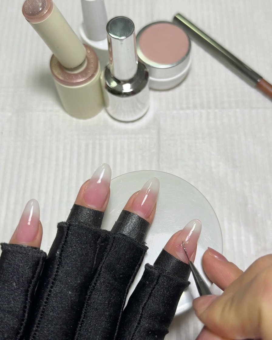 Un pennello liner sottile disegna le linee intersecanti di una stella usando gel cat-eye rosa su ununghia bianco latte.