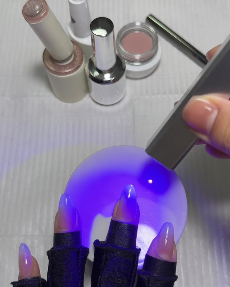 Una mano con unghie sotto una lampada UV, con il pollice che viene polimerizzato dopo che il design a stella cat-eye è terminato.