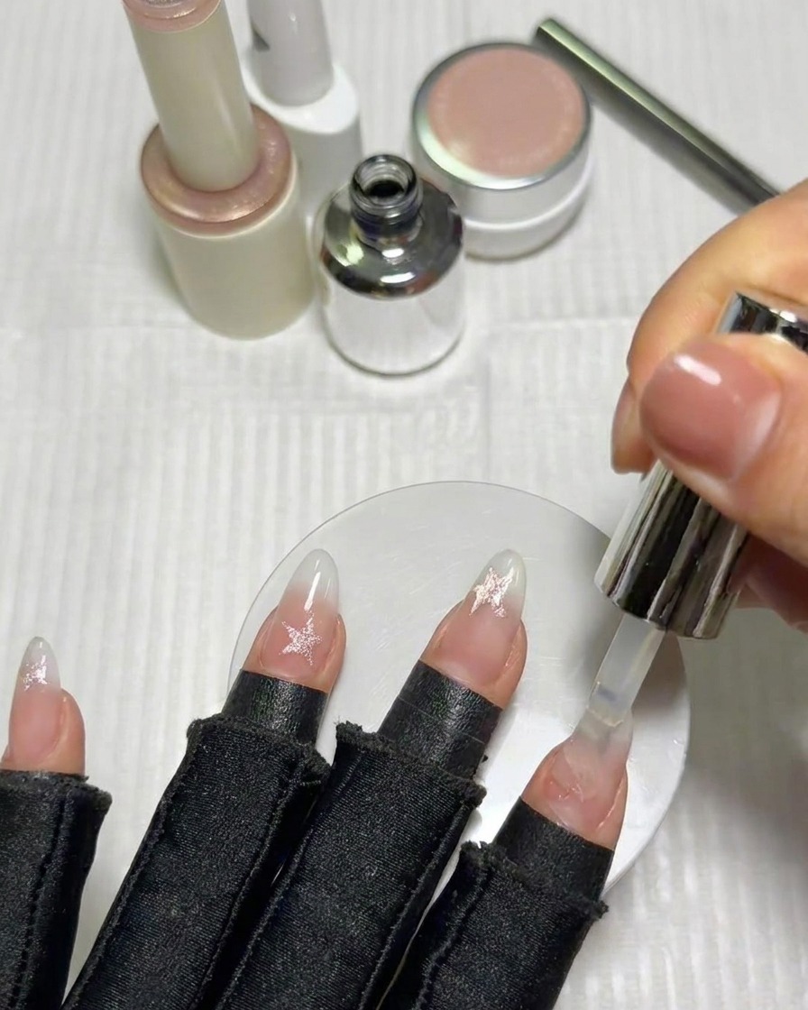 Un pennello applica un top coat lucido finale sopra le unghie decorate con stelle completate.