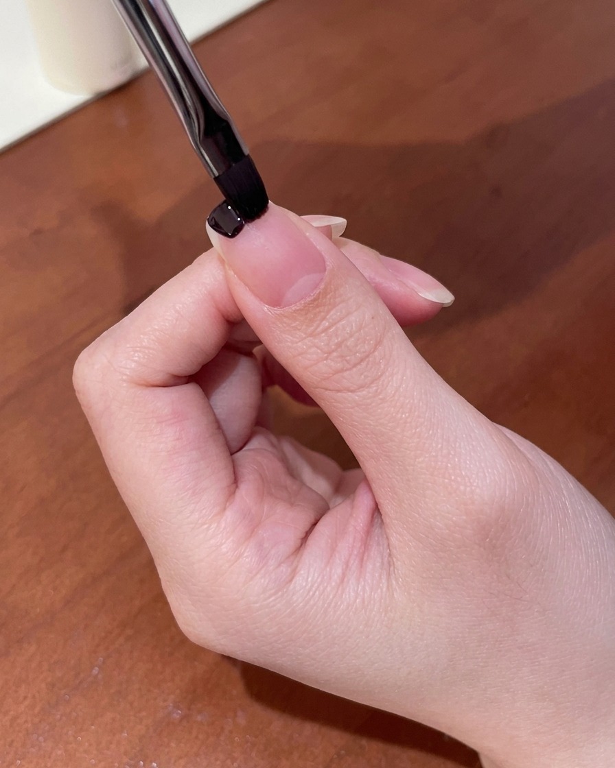 Primo piano di un piccolo pennello per gel che applica smalto viola scuro sulla punta dellunghia.