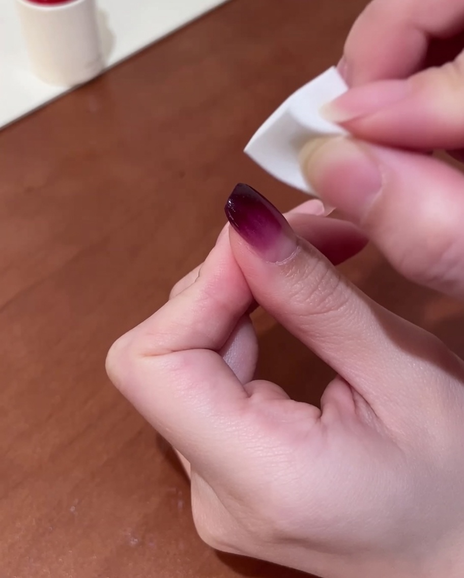 Primo piano di una mano che utilizza una piccola spugnetta per makeup, tamponando delicatamente lo smalto viola sullunghia per creare una sfumatura.