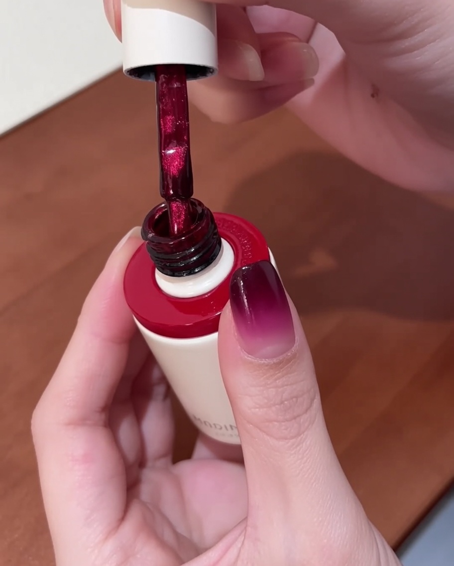Un pennello che applica smalto gel cat-eye rosso brillante su ununghia che ha già una base sfumata.