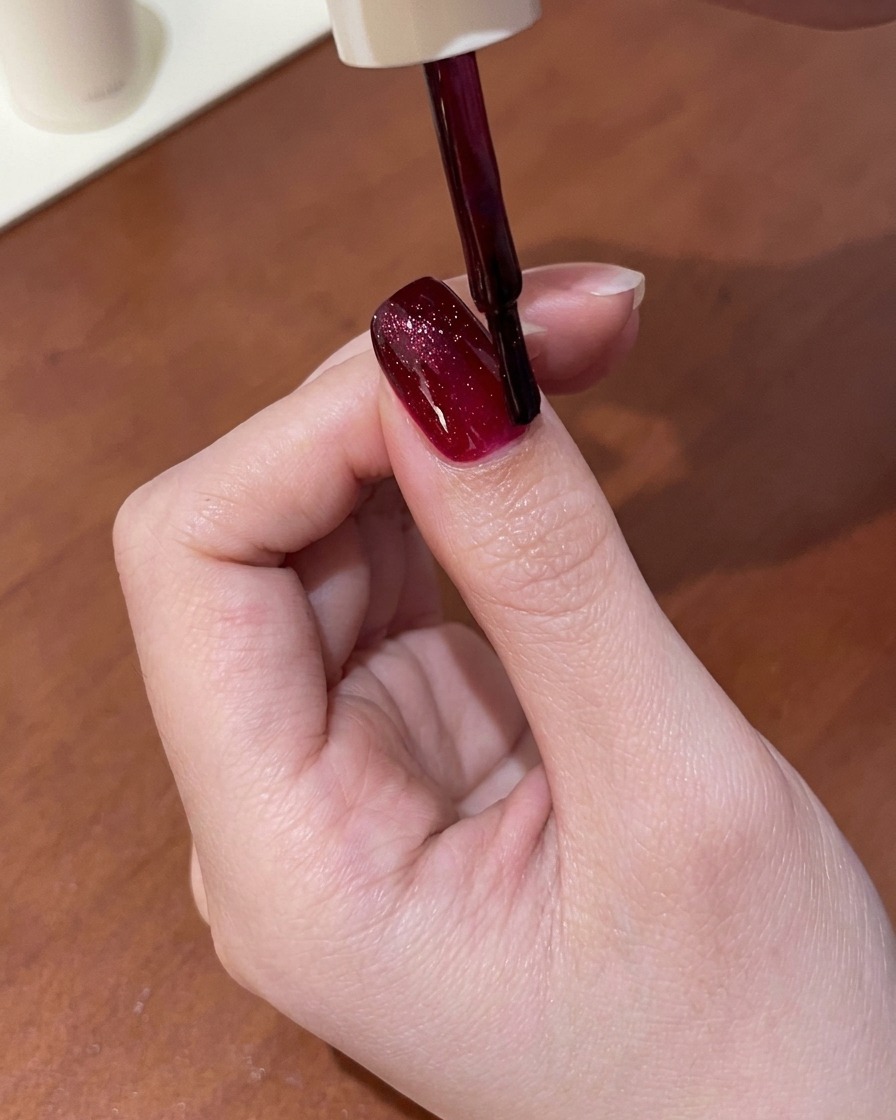 Uno strumento magnetico tenuto sopra ununghia rivestita di gel cat-eye rosso ancora umido, che attira il riflesso in una linea luminosa.