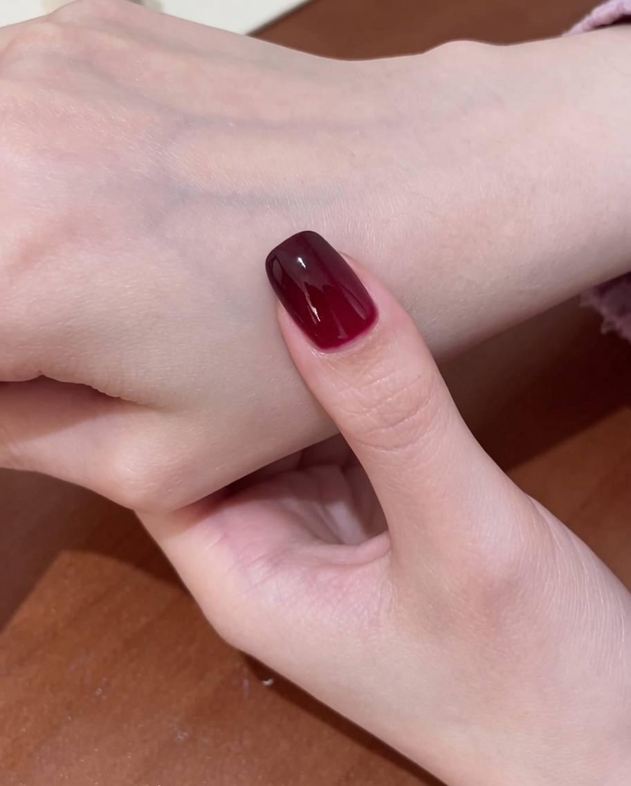 Un pennello che applica un top coat trasparente e lucido sopra il design finito delle unghie cat-eye rosse.