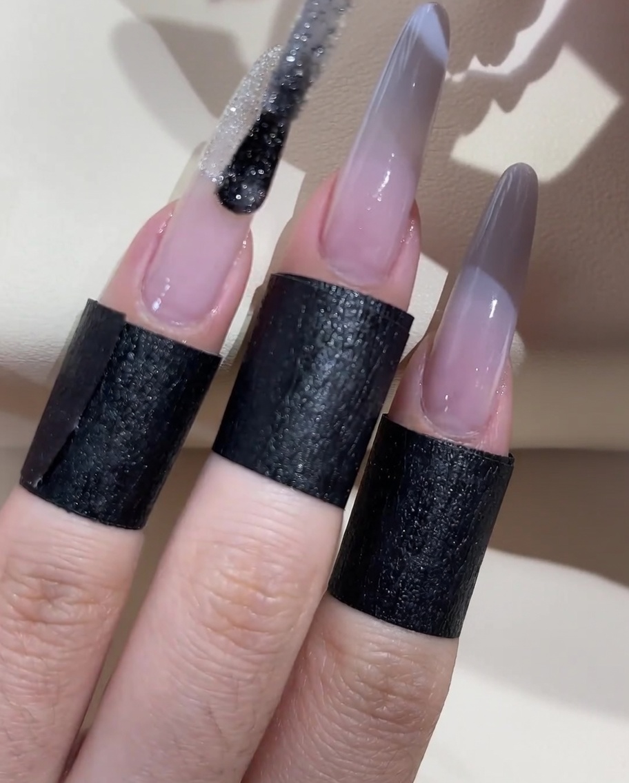 Un pennello che applica una linea di smalto glitter argento stellato attraverso il centro della transizione ombré.
