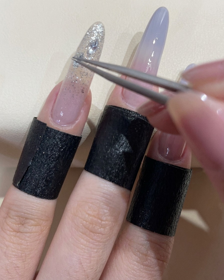 Una pinzetta che posiziona uno strass trasparente scintillante su ununghia coperta di gel adesivo umido.