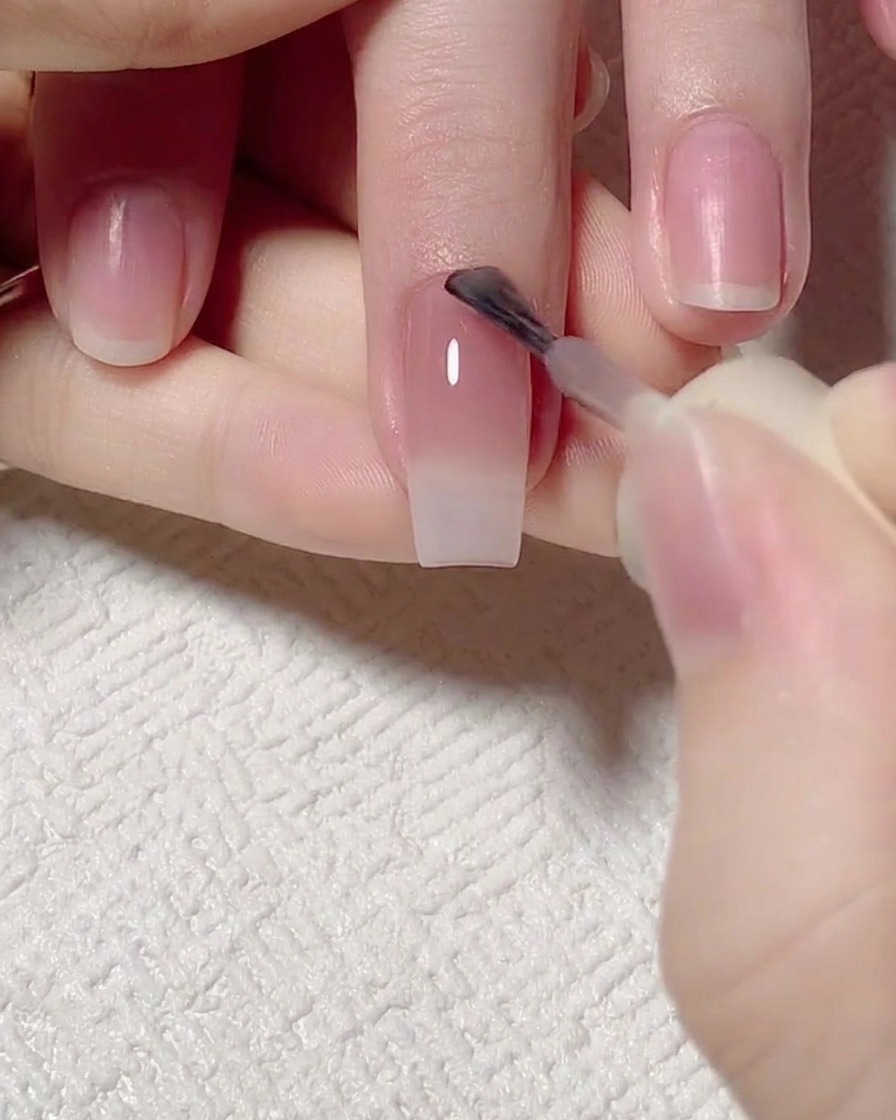 Un pennello che applica un gel rosa con riflessi giada sulla zona delle cuticole.