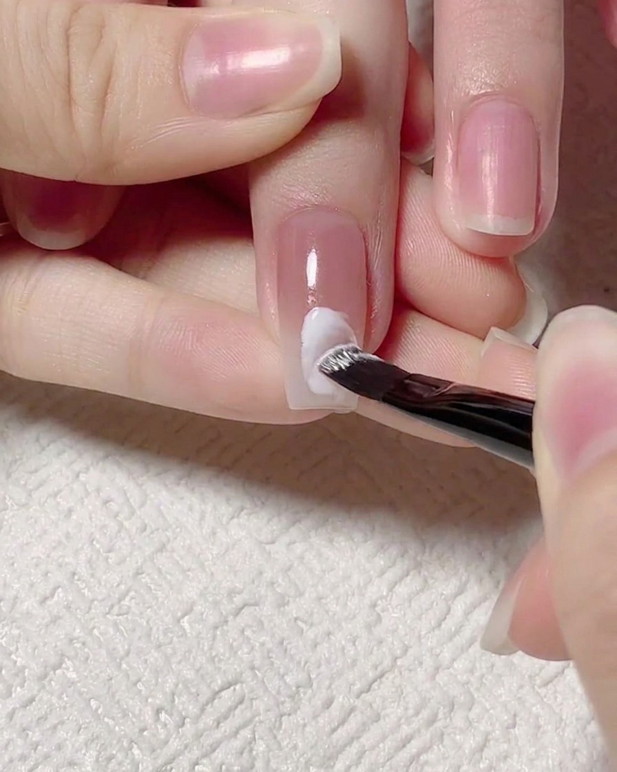 Un pennello di precisione che dipinge una linea a onda bianca al centro di ununghia gel.